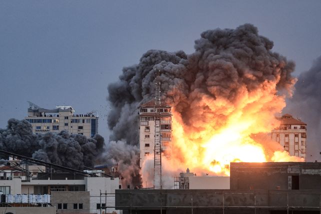 Personas paradas en una azotea observan cómo una bola de fuego y humo se eleva sobre un edificio en la ciudad de Gaza